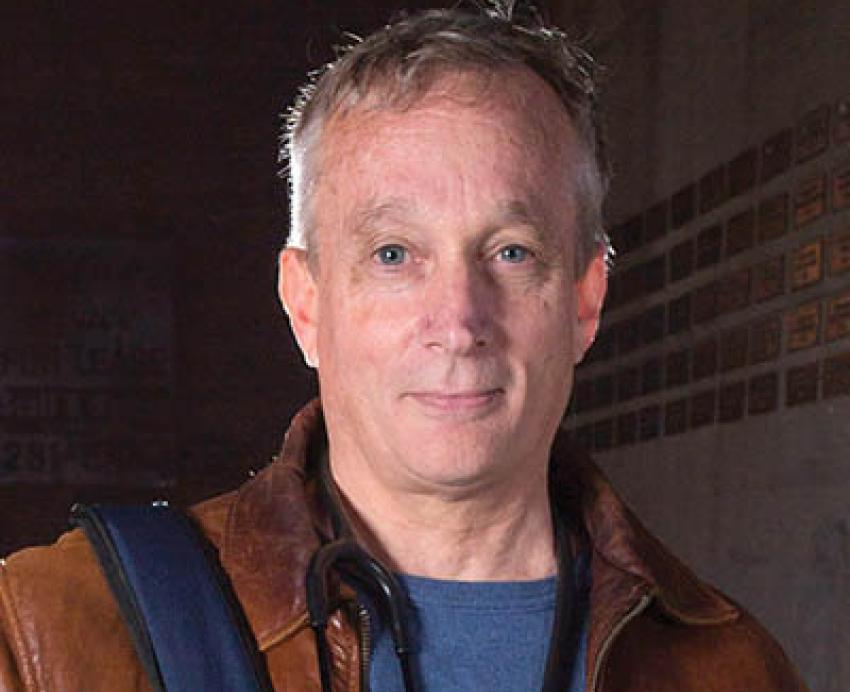 Jim Withers in a leather jacket holding a bag