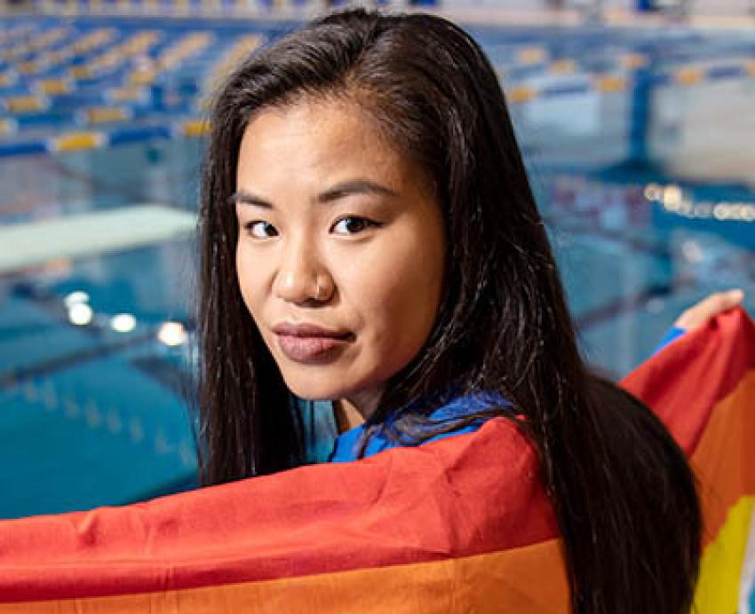Lisa Coe in front of a pool, holding a rainbow flag