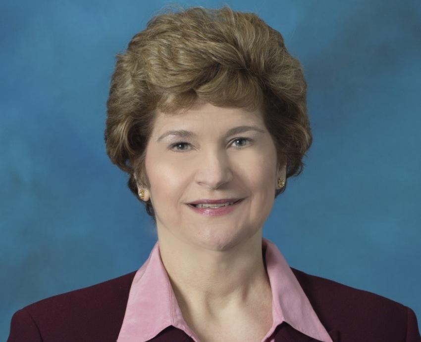 a woman in a pink collared shirt and black blazer in front of a blue photography background