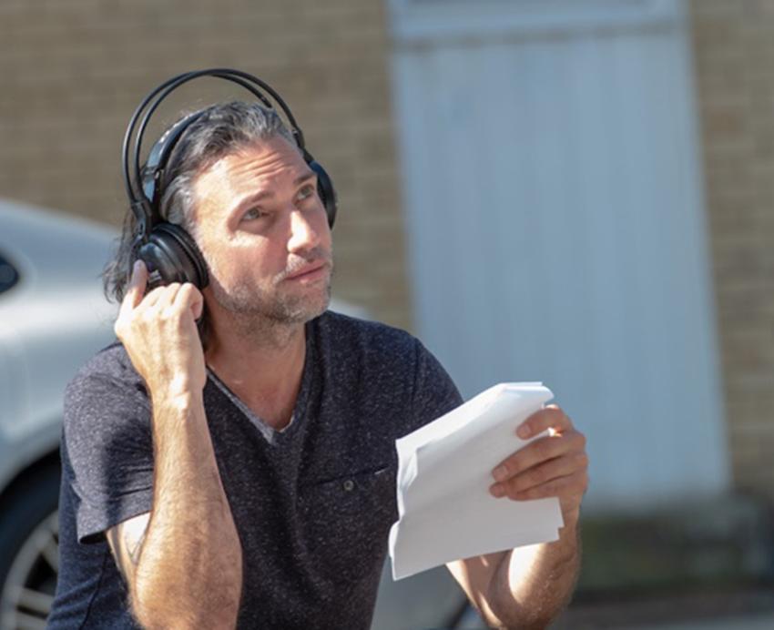 Paolo Pilladi in a dark shirt and headset, holding papers
