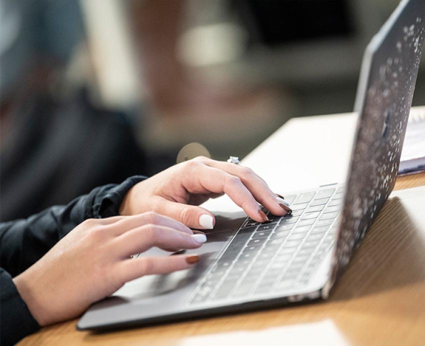 Person typing on grey laptop on wooden desk