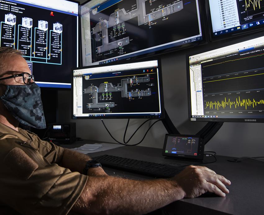 Man with mask using computer with five monitors