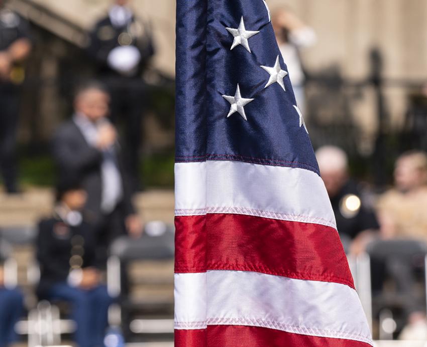 an American flag in the foreground with people gathered in the background