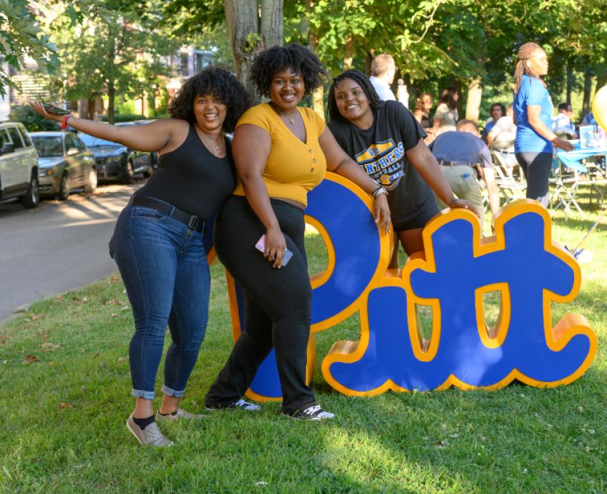 Three students sit on a Pitt display cutout