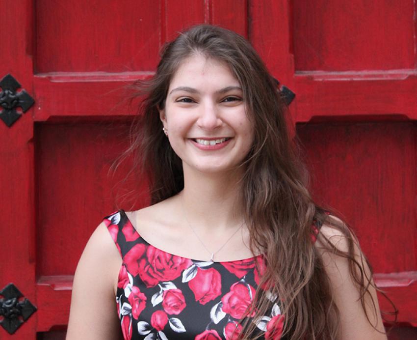 Sabrina Helbig wearing black and red dress, smiling in front of large red door 