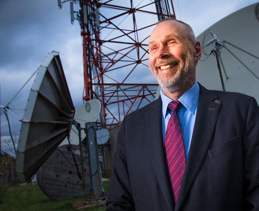 Martin Weiss wearing suit with red tie, standing in front of satellite dishes