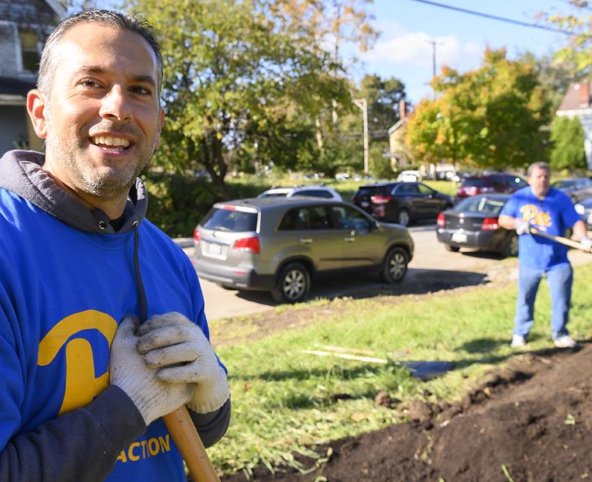 Two men with blue Pitt shirts digging dirt from ground.