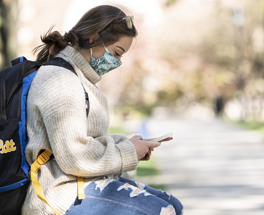 Student sitting outside on a bench using cell phone