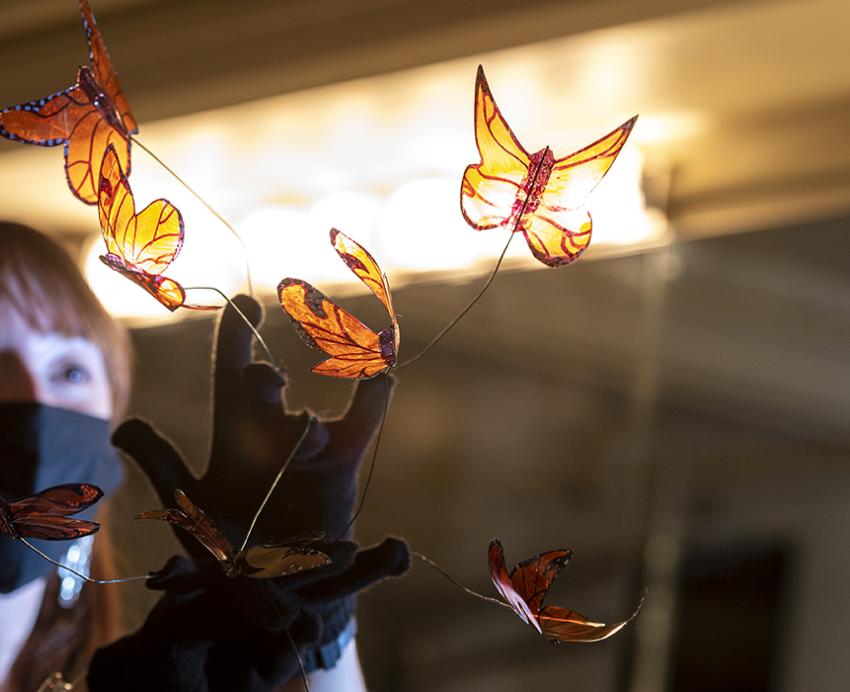 Woman with face mask holding plastic butterflies in front of light
