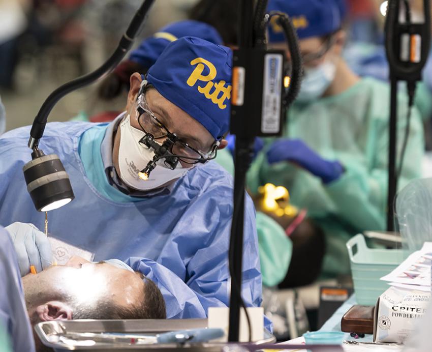 Pitt dentist wearing blue and gold Pitt cap working on patient