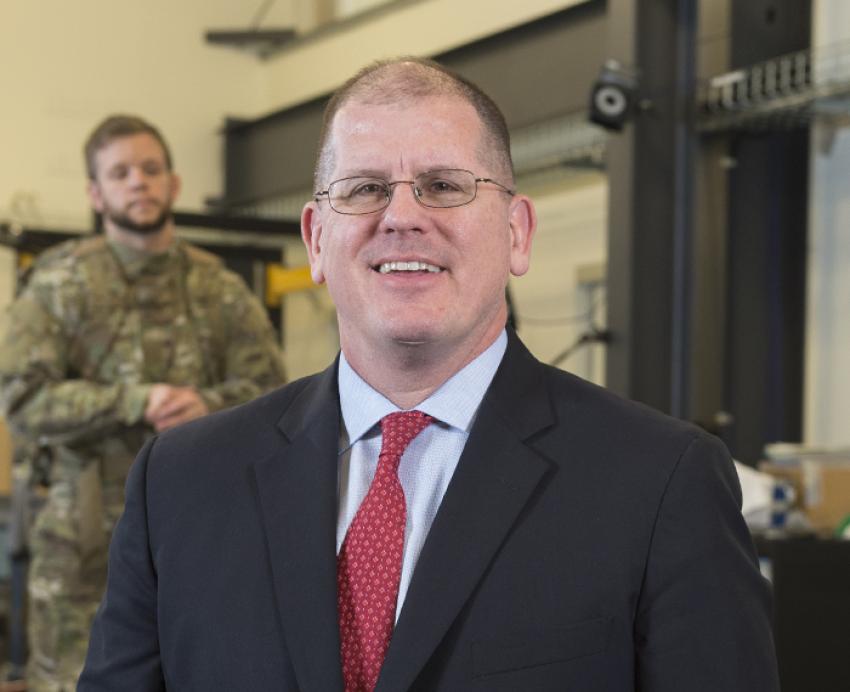 Brad Nindl smiling wearing black suit with read tie