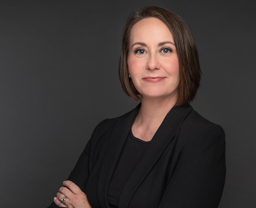 Lina Dostilio smiling with arms folded in front of grey background