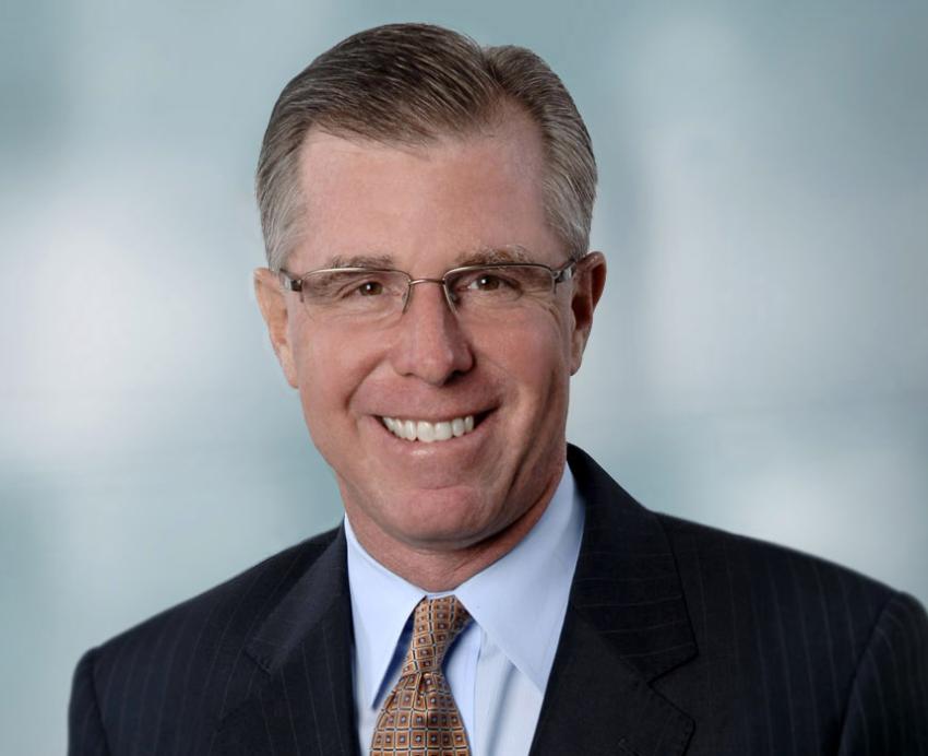 a man in a dark suit, blue shirt and gold tie