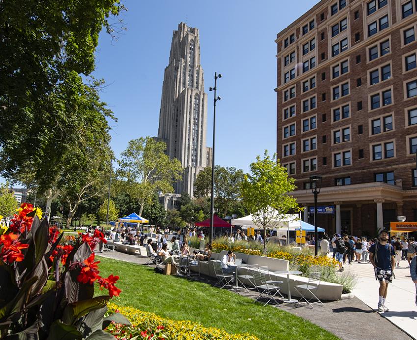 Cathedral of Learning towering behind flowerbed and busy sidewalk