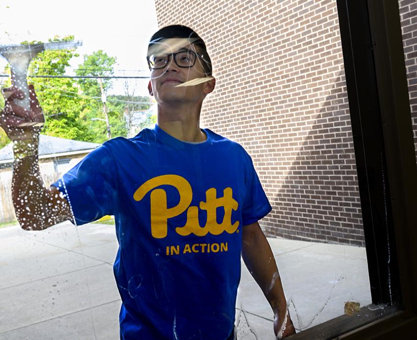 Man with blue Pitt shirt cleaning window from the outside