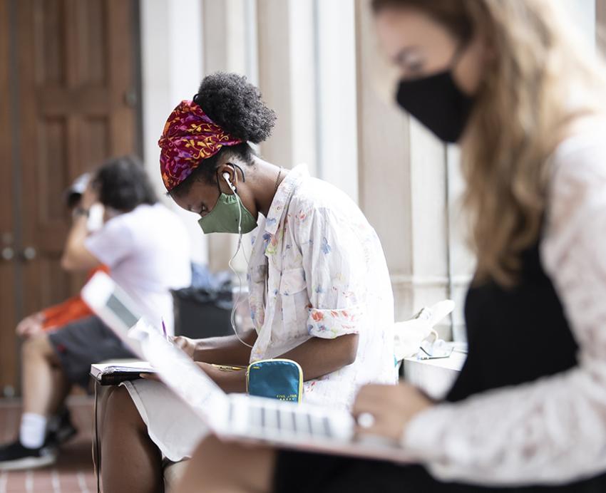 Multiple Pitt students with face masks studying separately on a long bench 