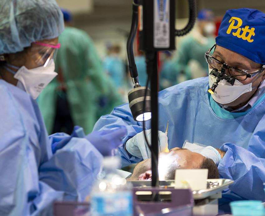 Dentist with blue Pitt cap working with assistant 