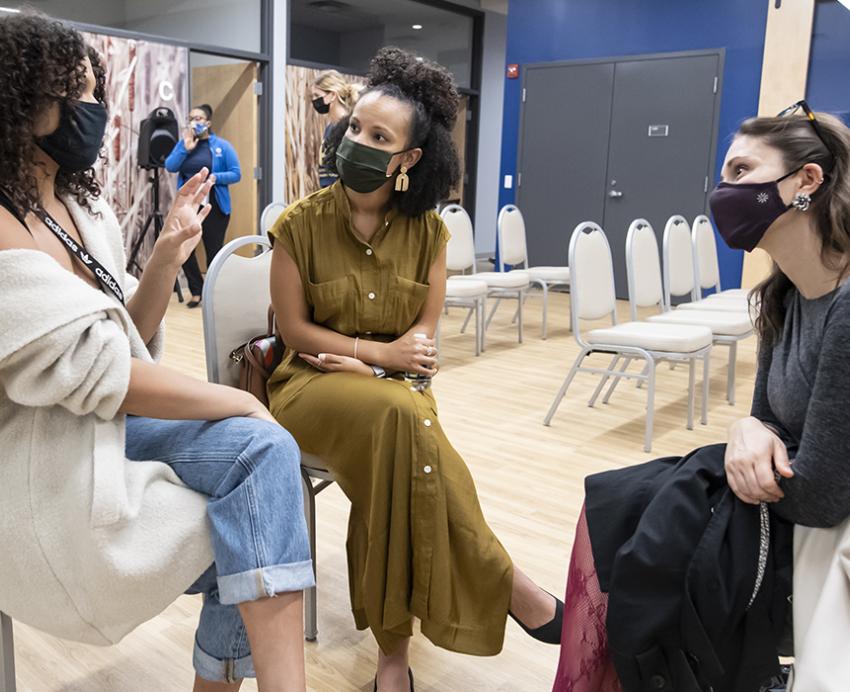 Three women talking to each other while sitting in chairs 