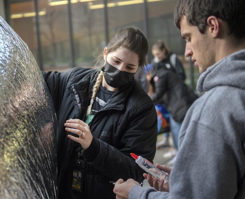 two students attaching something with glue to a silver balloon