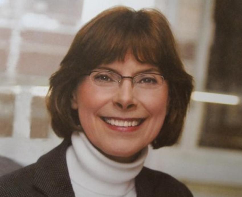 Beth McGrew smiling and wearing white turtleneck and black jacket 