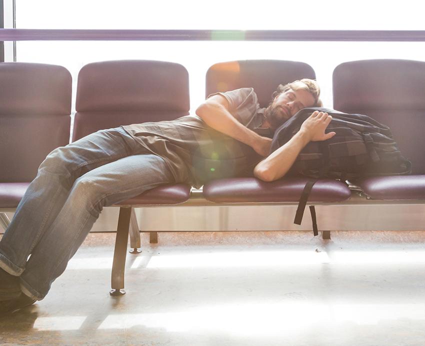 Man sleeping on chairs with head on backpack in airport