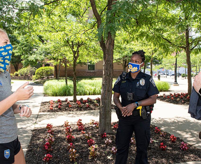 Two police officers in face masks talk to a person in a gray t-shirt and shorts