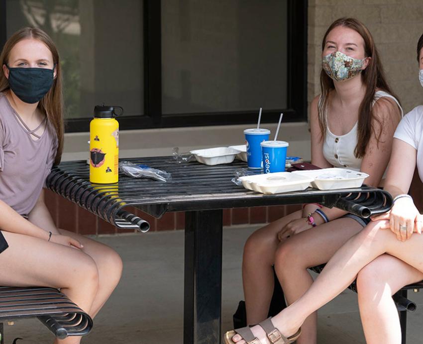 Three women with face masks sitting at a table outside