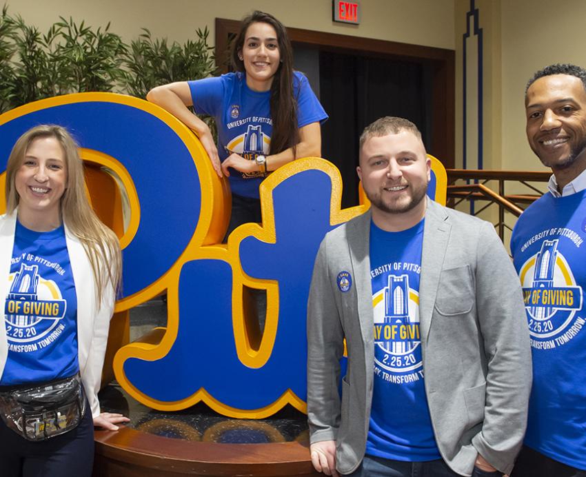 Roc posing with people wearing Pitt Day of Giving shirts next to Pitt sign