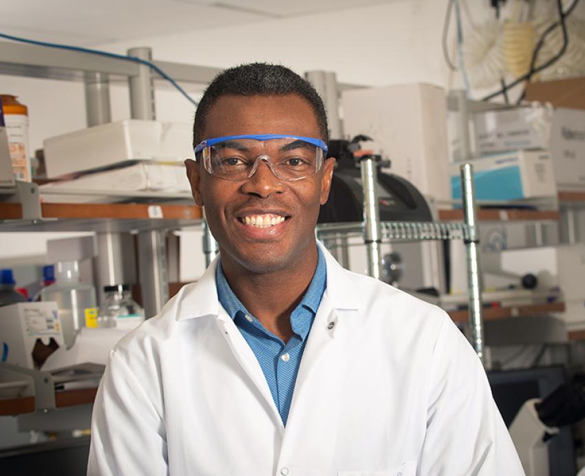 Tagbo Niepa wearing lab coat and safety goggles