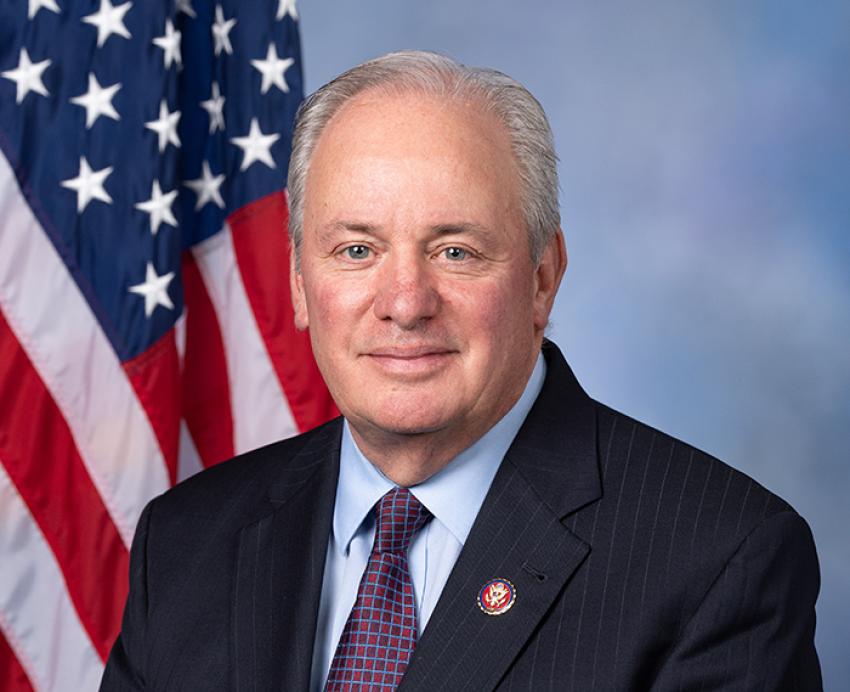Mike Doyle wearing a black suit in front of an American Flag
