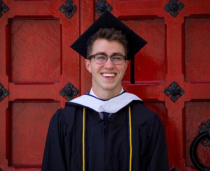 Chandler Mitchell wearing cap and gown in front of large red door