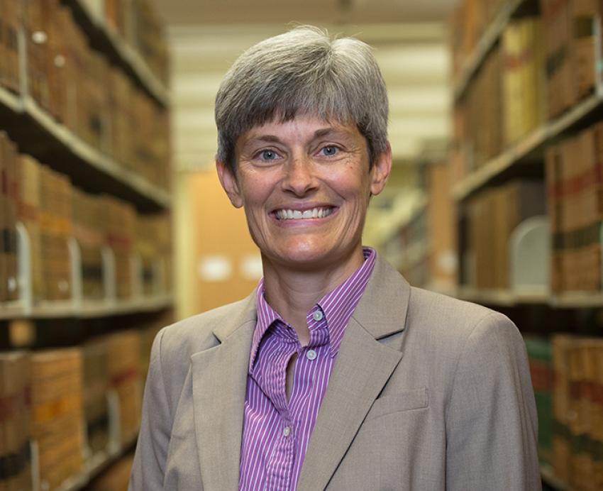 Amy Wildermuth in tan blazer standing next to bookshelves