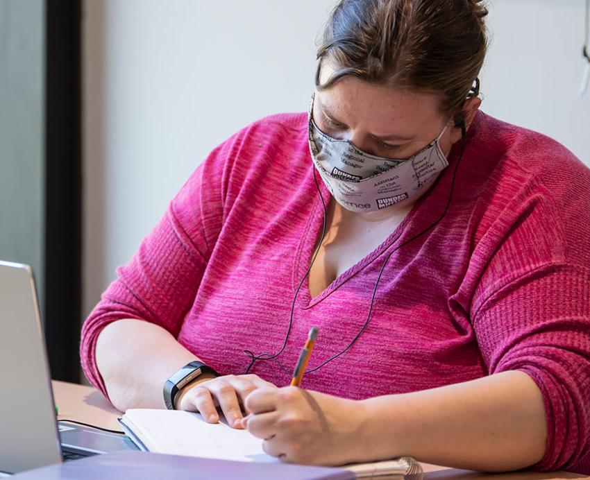 a person in a pink blouse studying at a laptop
