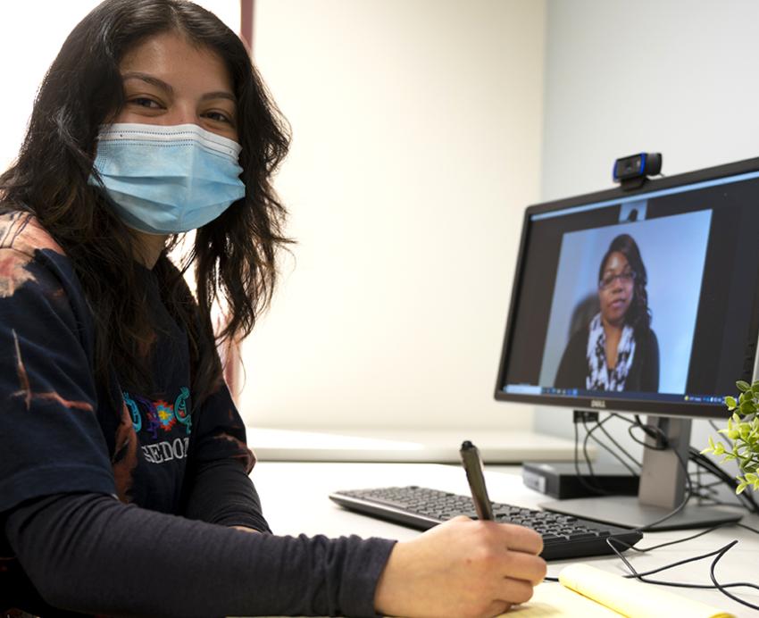 Woman sitting at desk and writing notes during video call