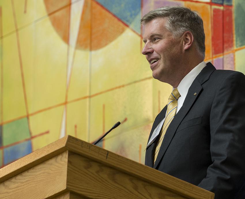Chancellor Patrick Gallagher speaking at podium in front of colorful wall