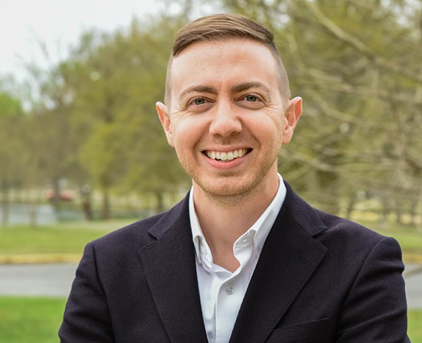 Michael Davila wearing black suit outside in front of trees