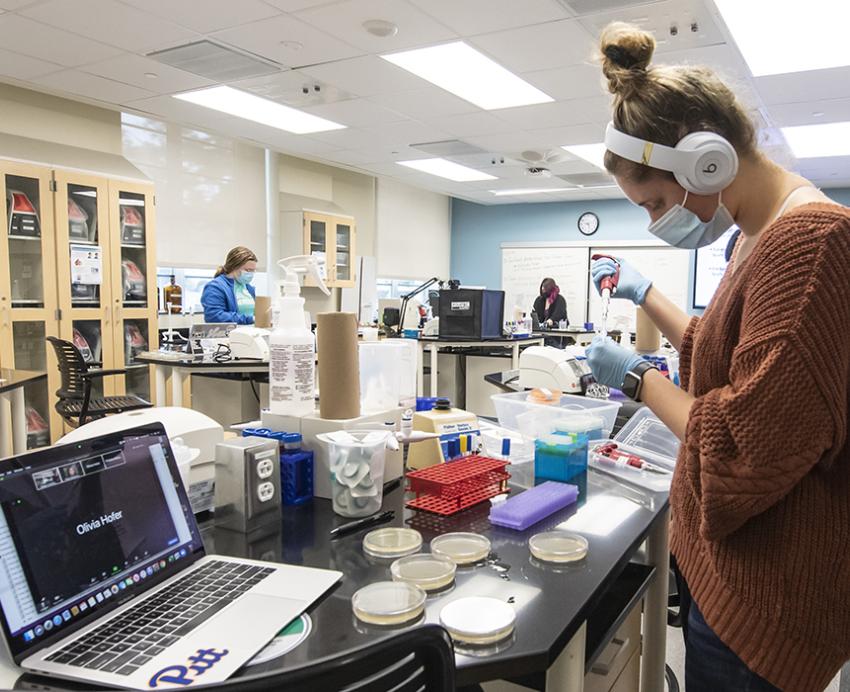 A person wearing headphones and a face mask in a brown sweater performs tests at a desk