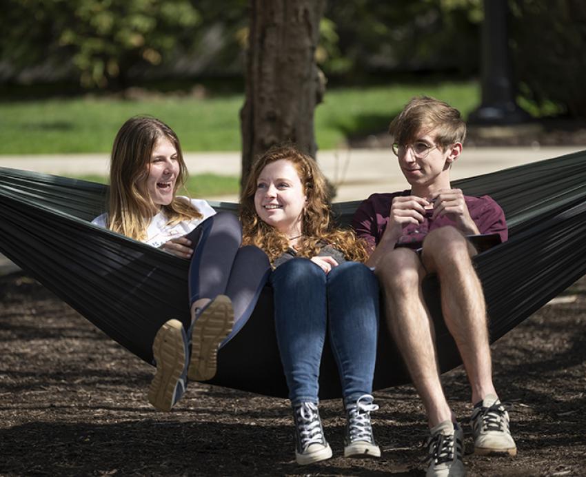 Three students sitting on hammock together