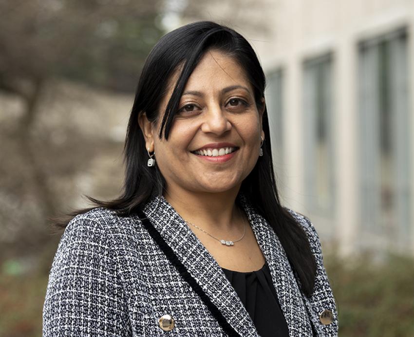 Manisha Jhamb smiling in grey suit outside