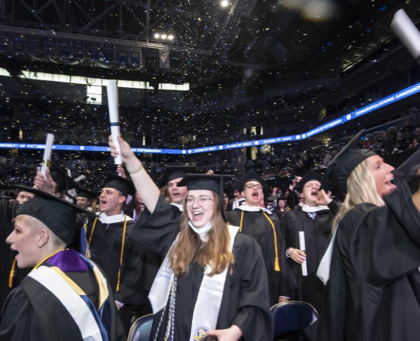 Pitt graduates cheering and holding diplomas in the air