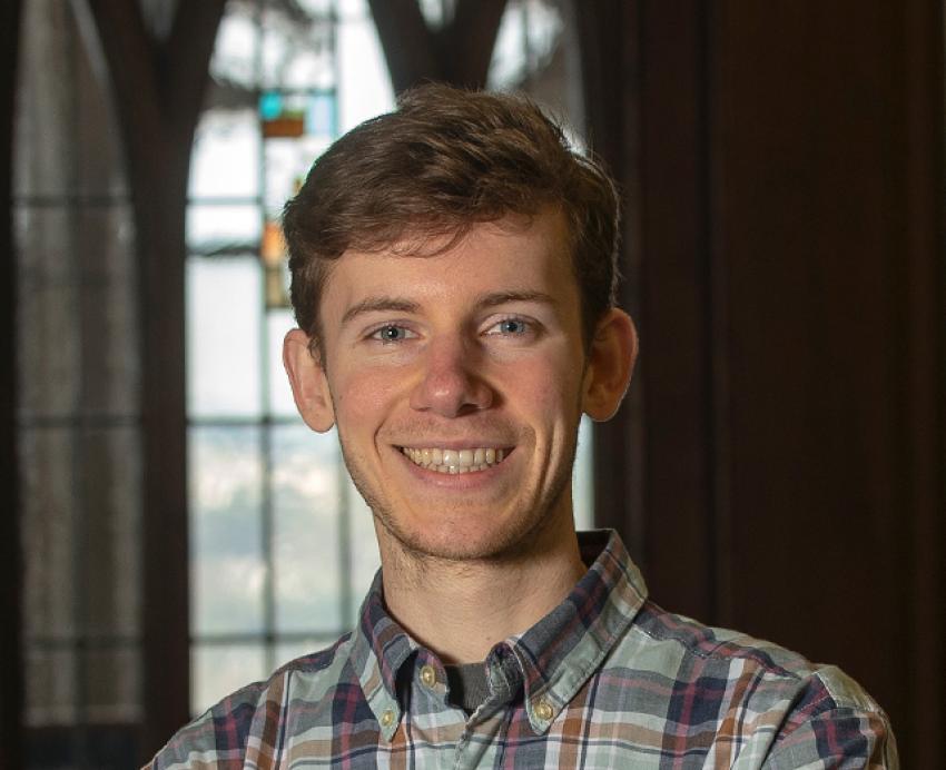 Asher Hancock smiling in plaid shirt with arms folded