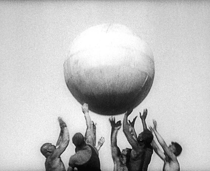 Black and white image of several people reaching up for large ball