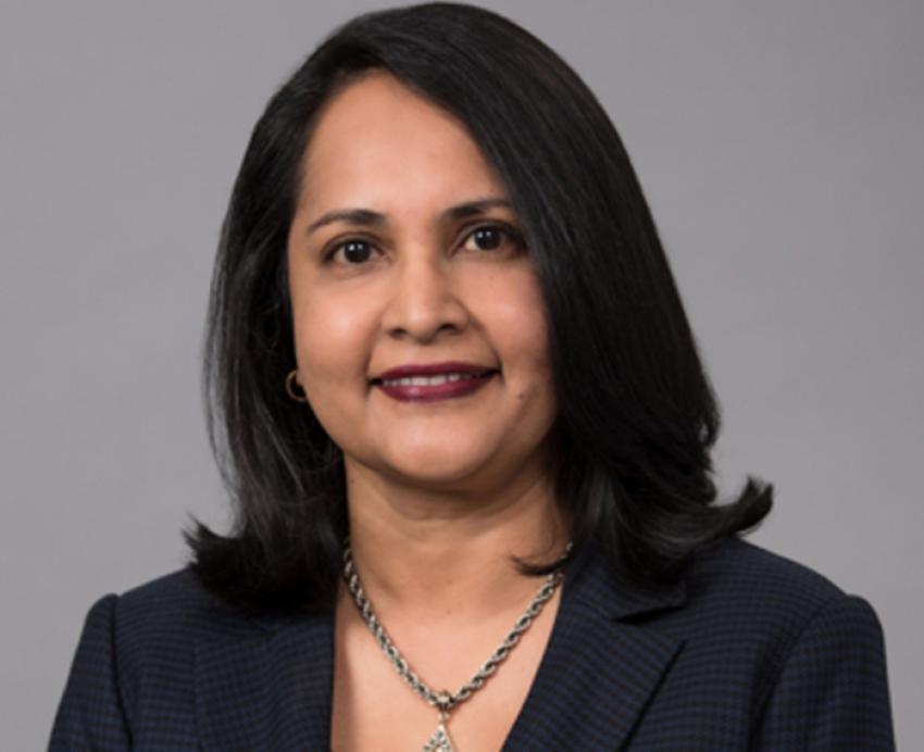 Vanitha Swaminathan smiling in black suit in front of grey background