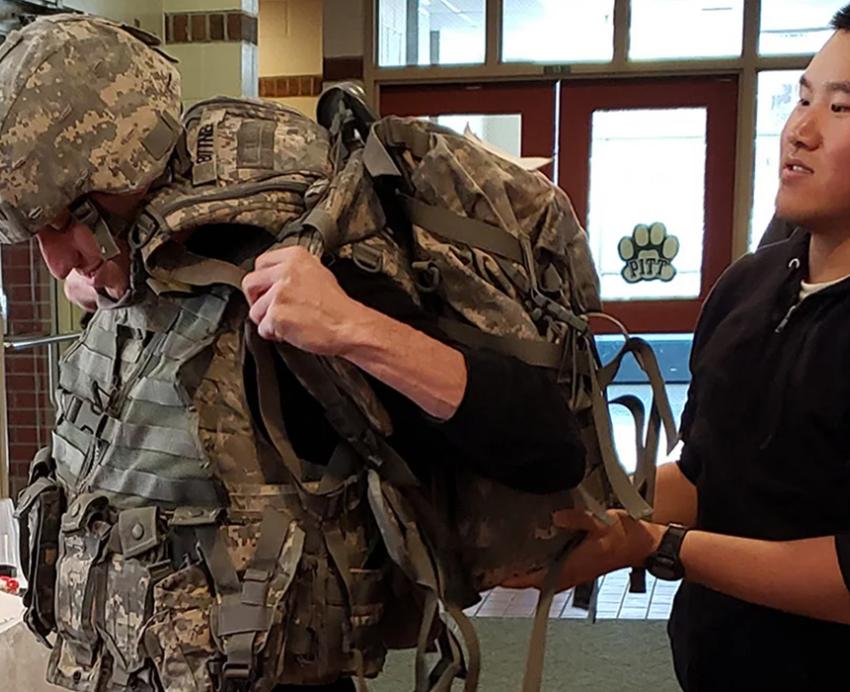 a person helping someone lift up a camo backpack