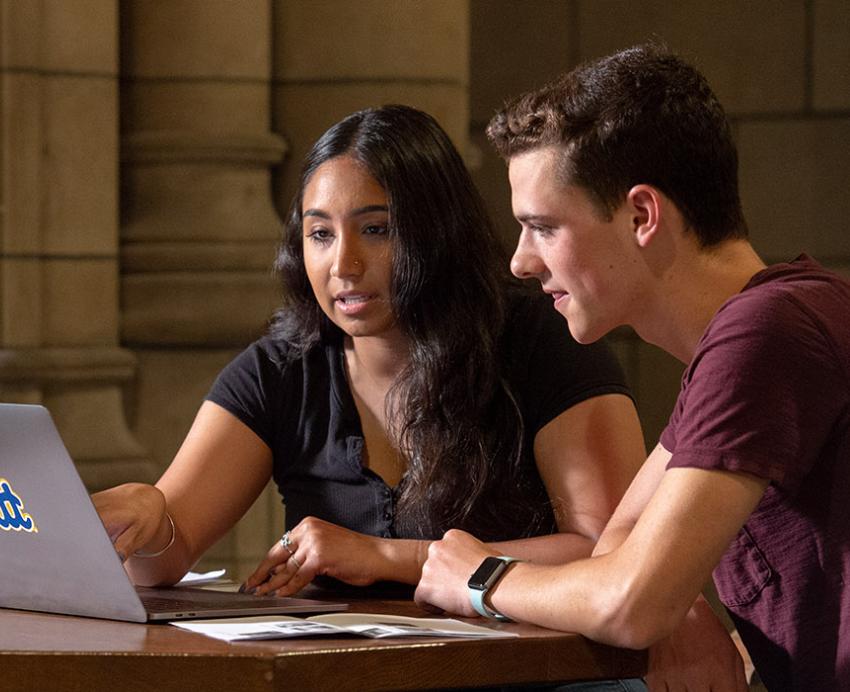 two students at a laptop with a Pitt sticker on it