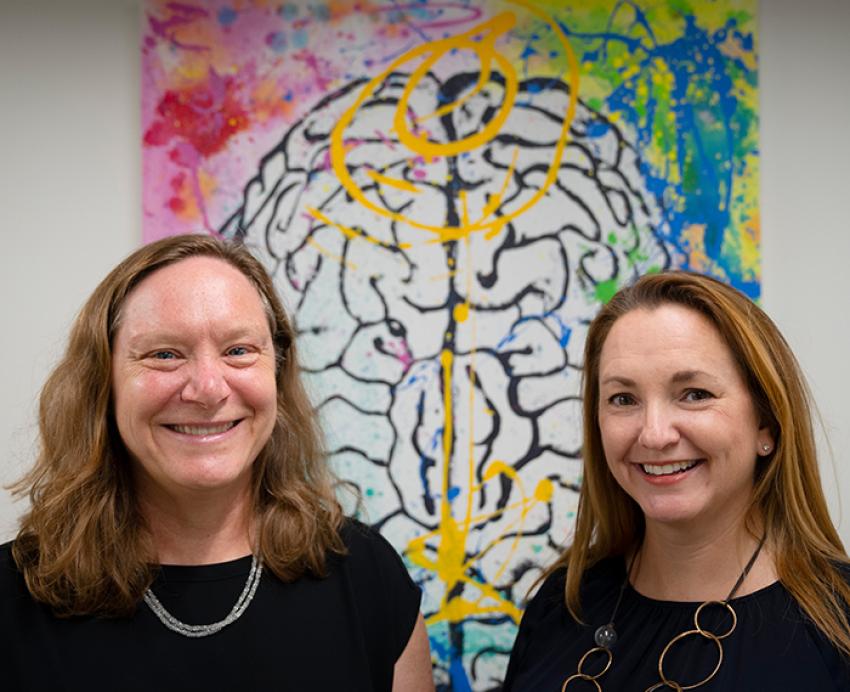 the two new leaders in front of a colorful illustration of a brain