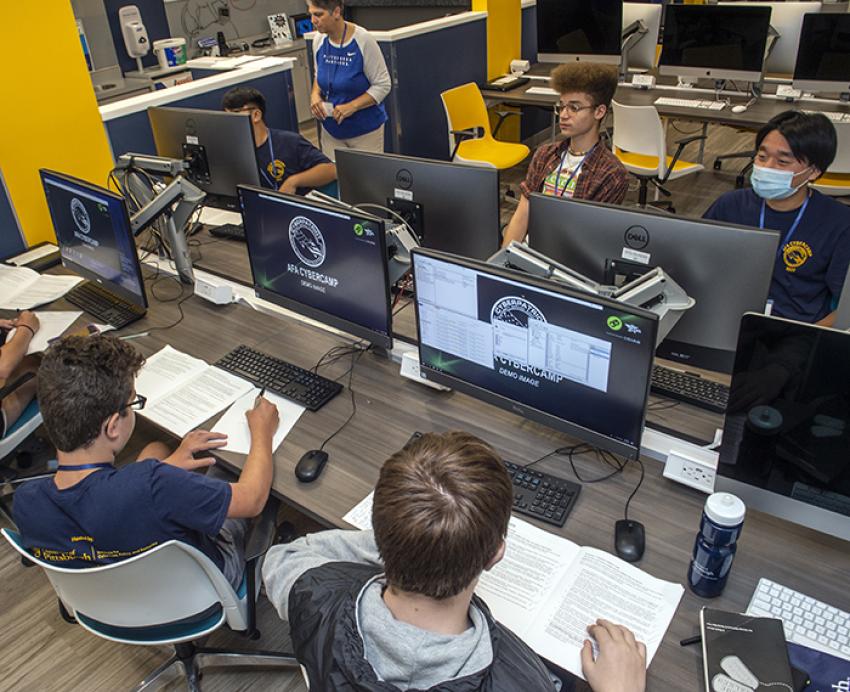 several kids at large computers with books in front of them