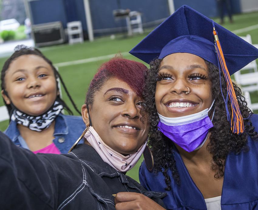 students taking a selfie, one dressed in graduation regalia