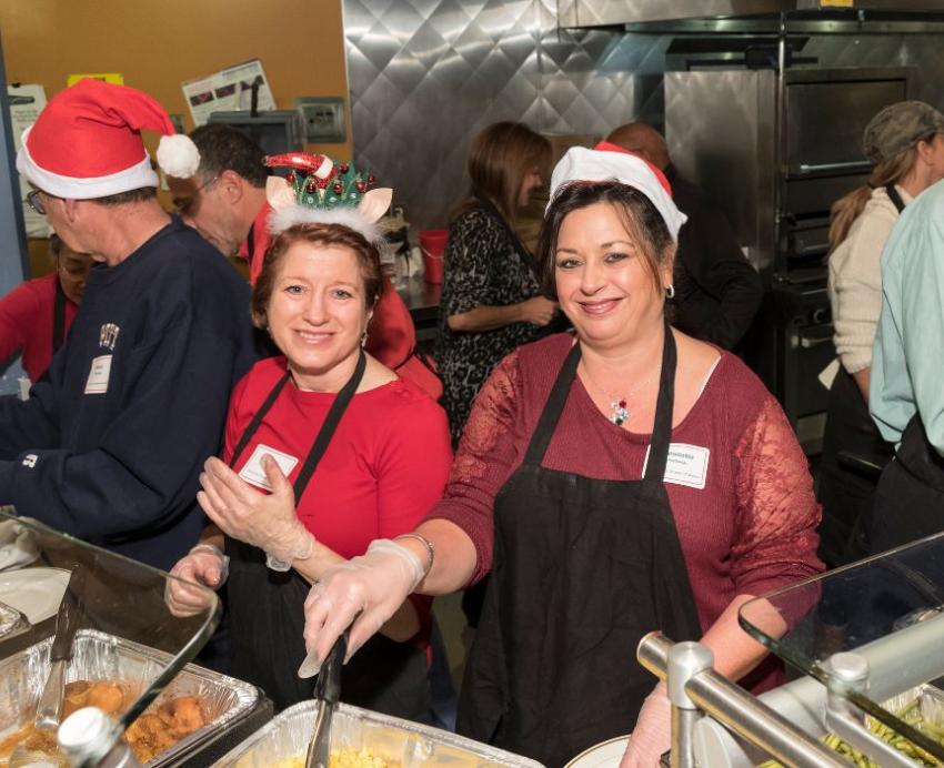 Volunteers wearing Santa hats serve food from trays.