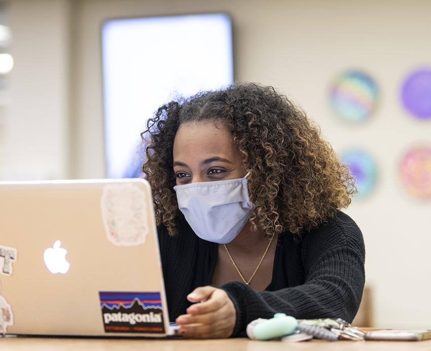 A student wearing a mask looks at a MacBook.